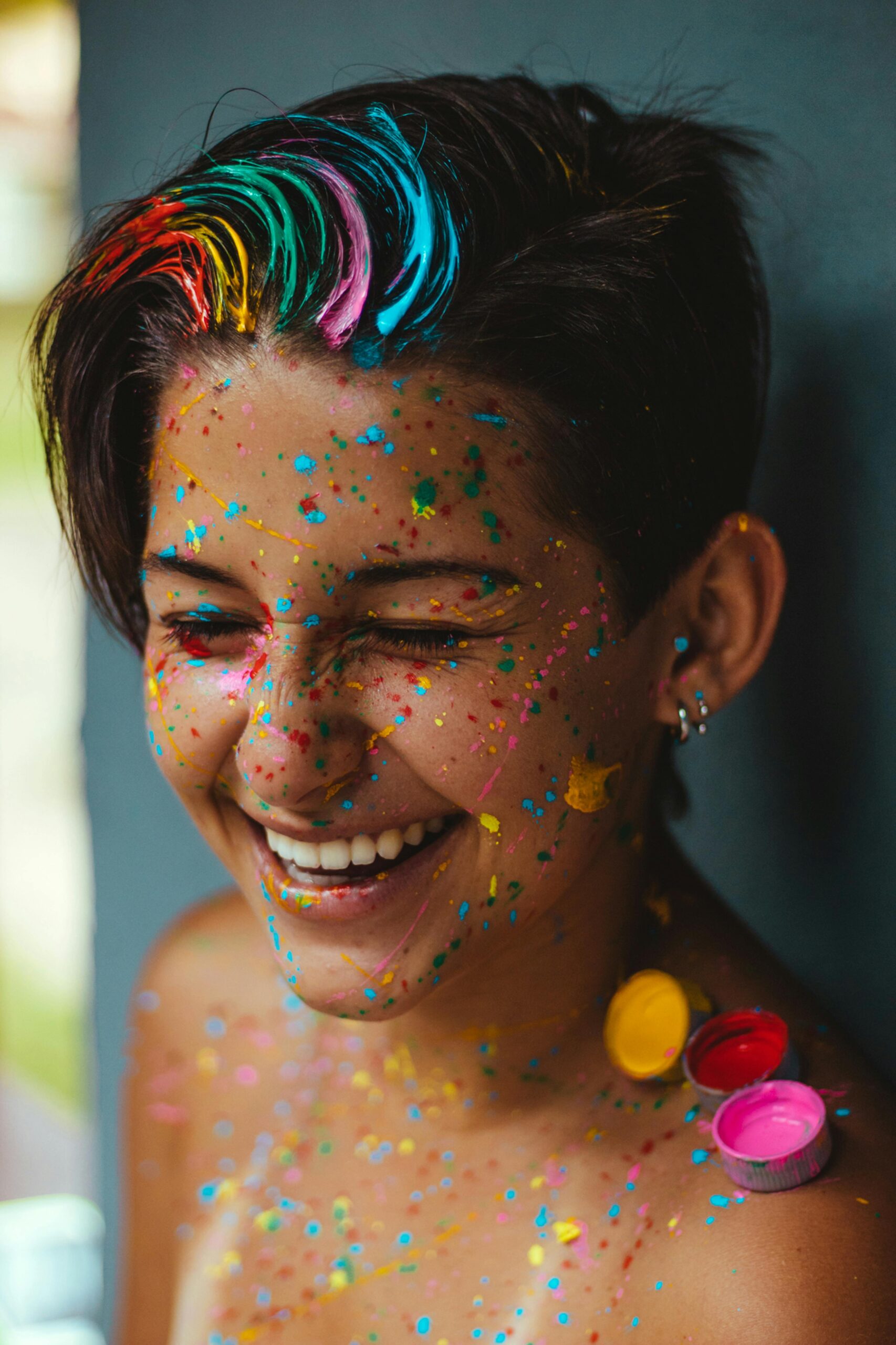 Smiling woman with vibrant face paint and colorful confetti, celebrating happiness and creativity.